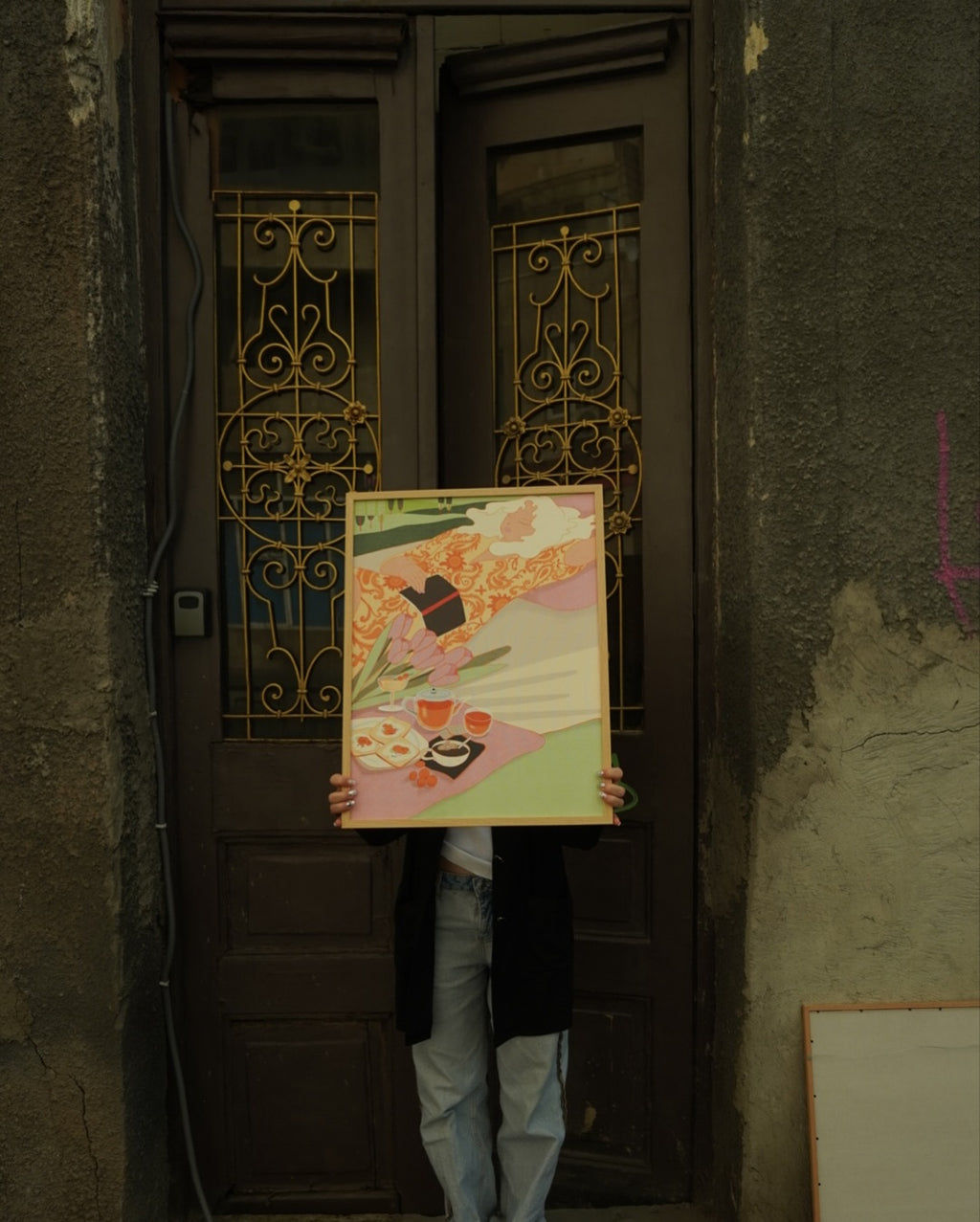 Person holding the framed “Savoring the Sunshine” art poster in front of an ornate doorway.
