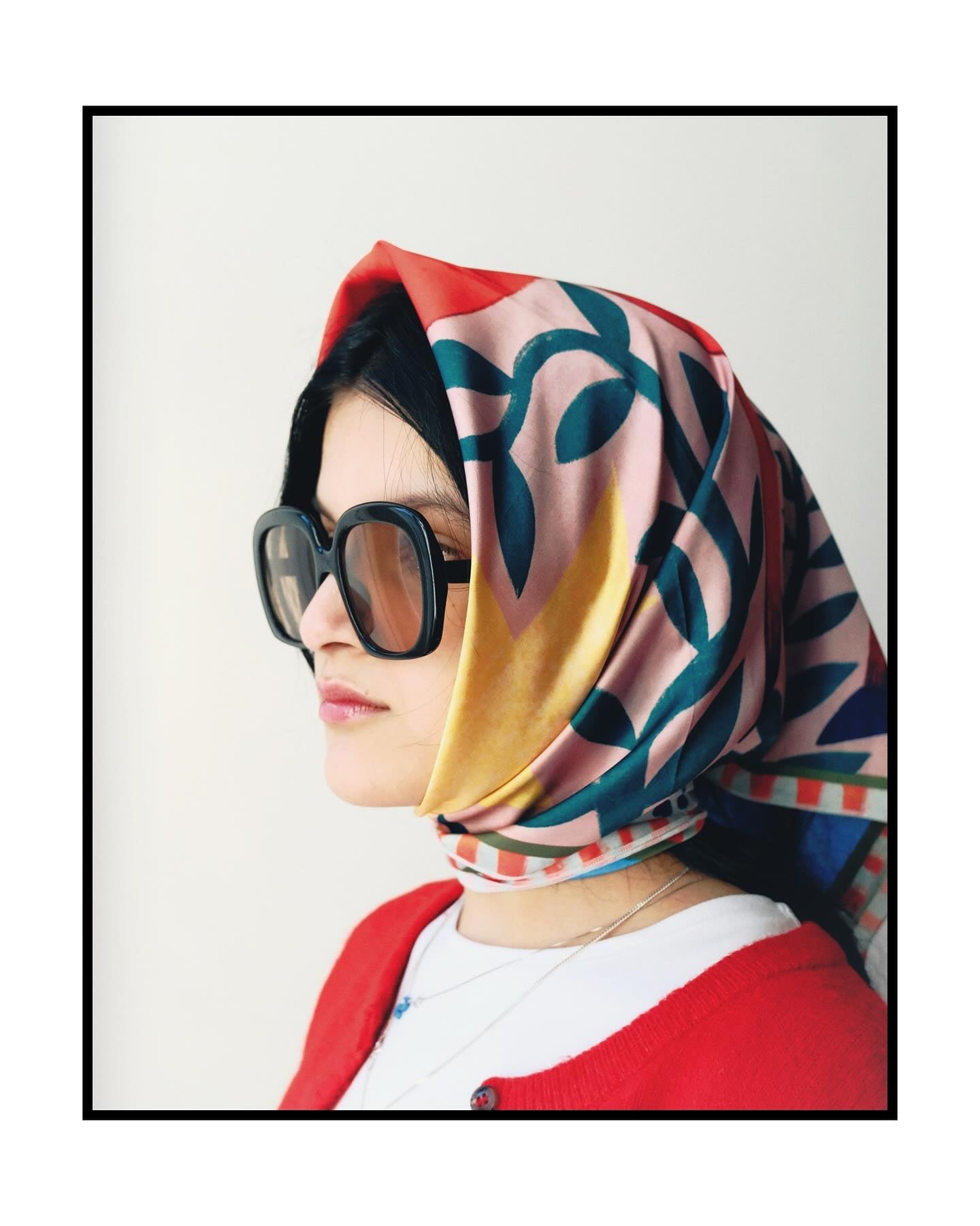 Person wearing a colorful scarf by DAE and sunglasses on a plain background