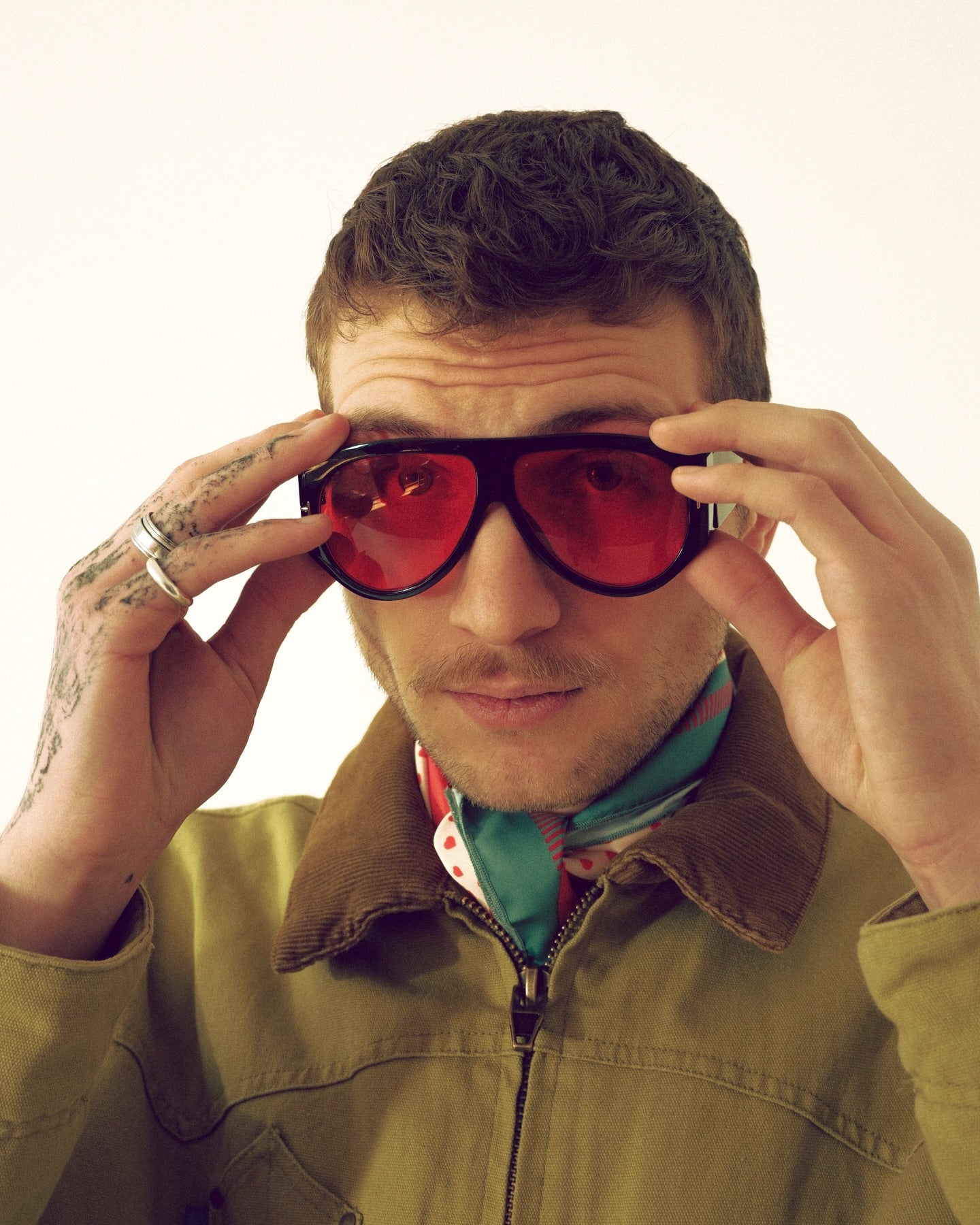 Man wearing a green jacket and red sunglasses with a neutral background, DAE's scarf on the neck
