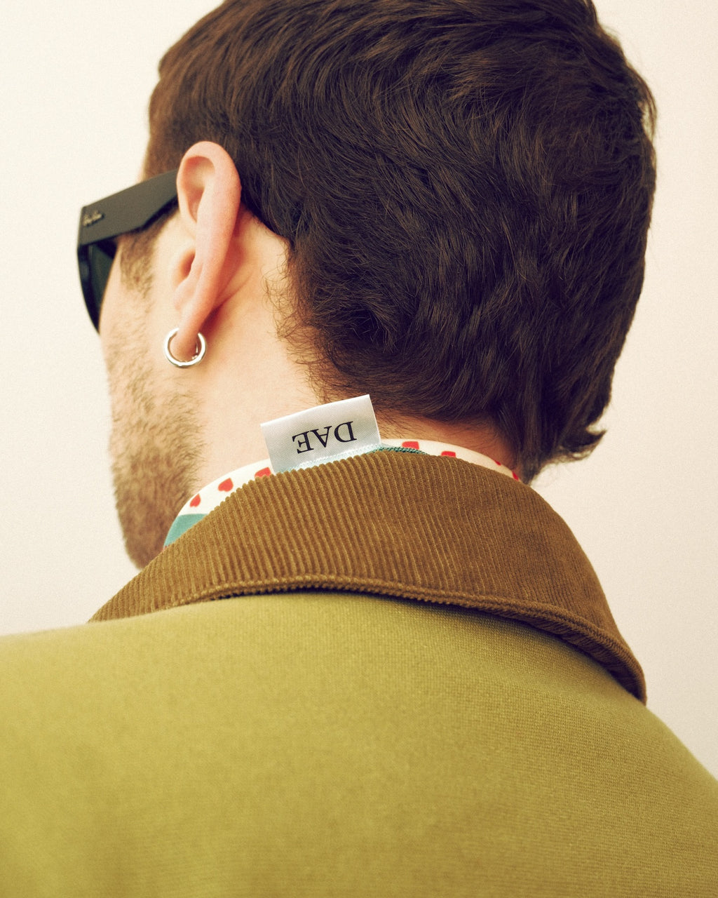 Person wearing a green coat with a visible brand tag, standing against a plain background.