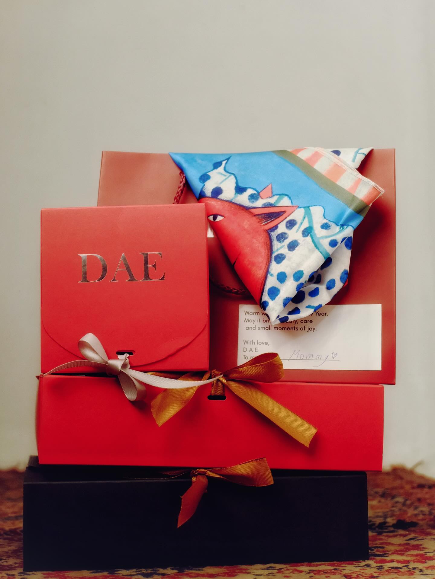 Red gift box with a bow and patterned scarf on a neutral background