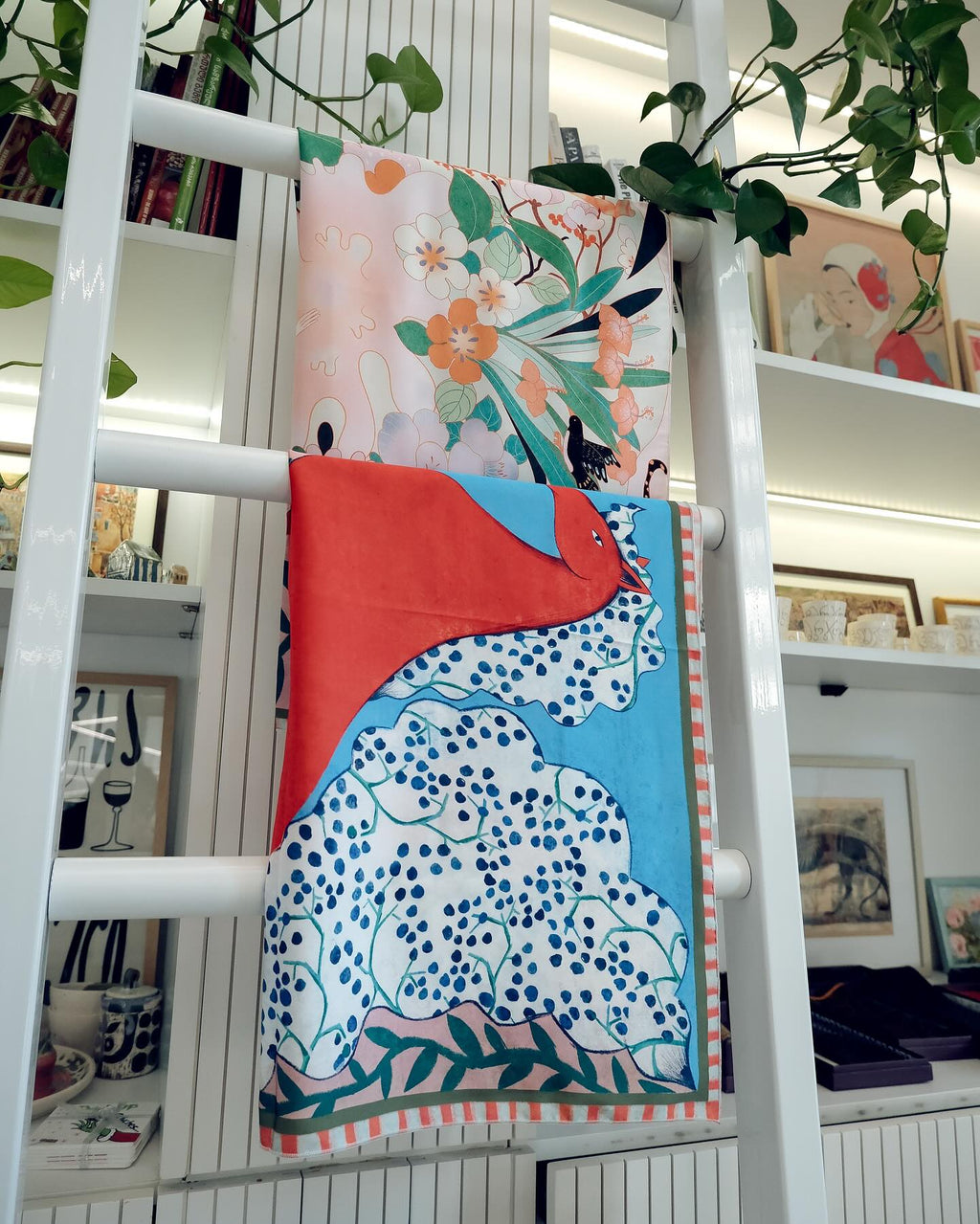 Colorful scarf with floral and abstract patterns draped over a white ladder in a store setting.