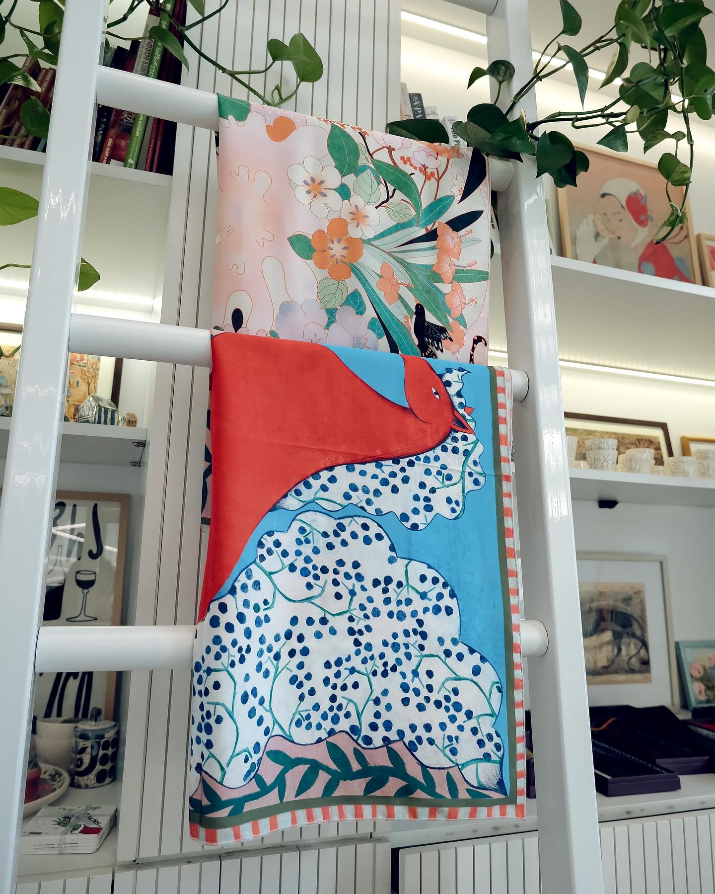 Colorful scarf with floral and abstract patterns draped over a white ladder in a store setting.