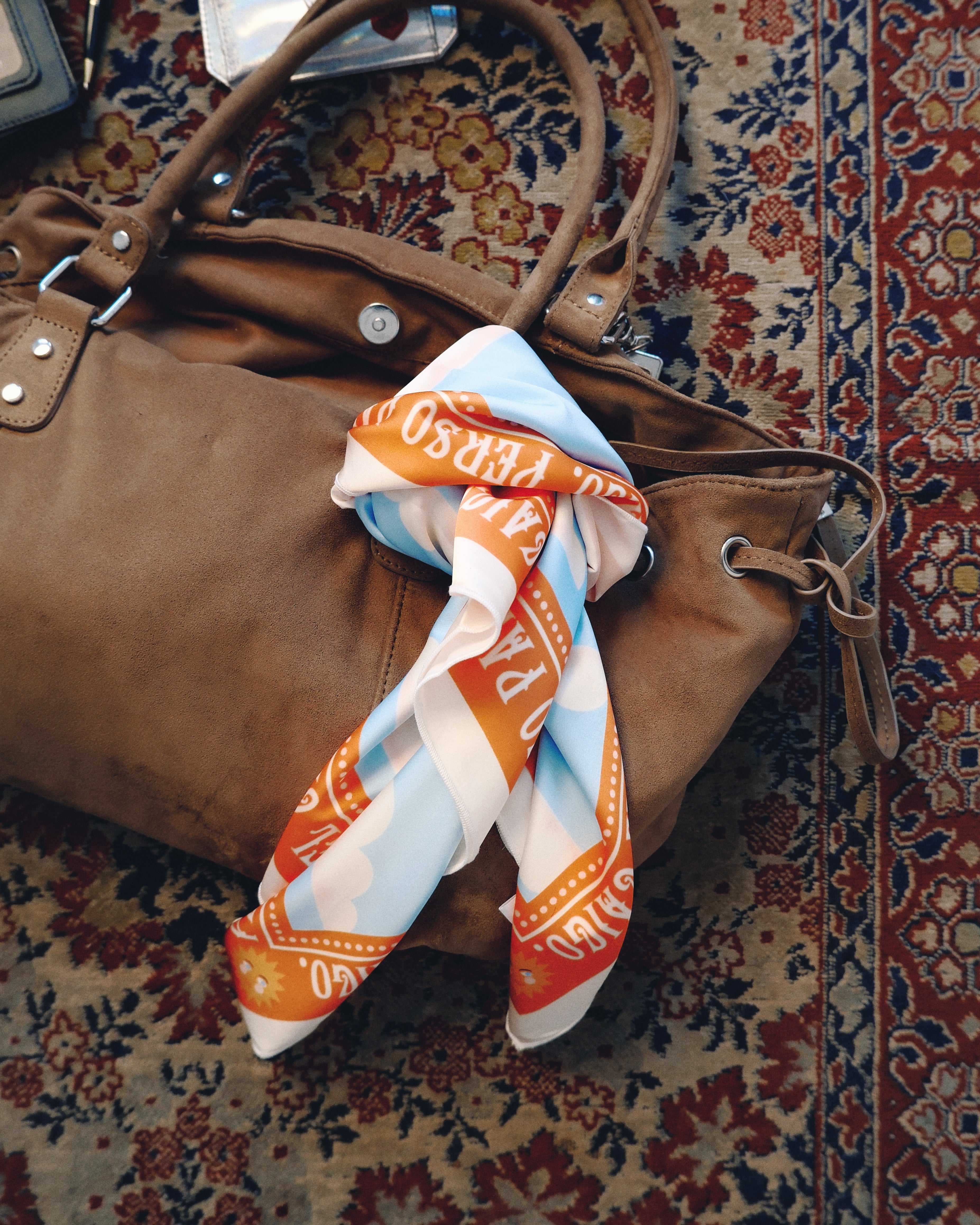 Brown handbag with a colorful scarf draped over it on a patterned rug
