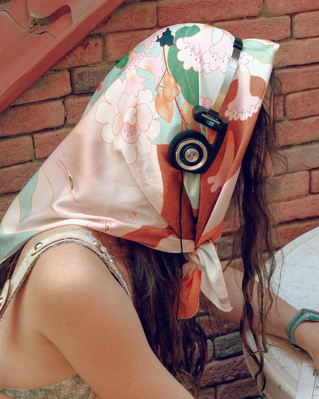 Person wearing a colorful scarfwith floral and nature design against a brick wall.