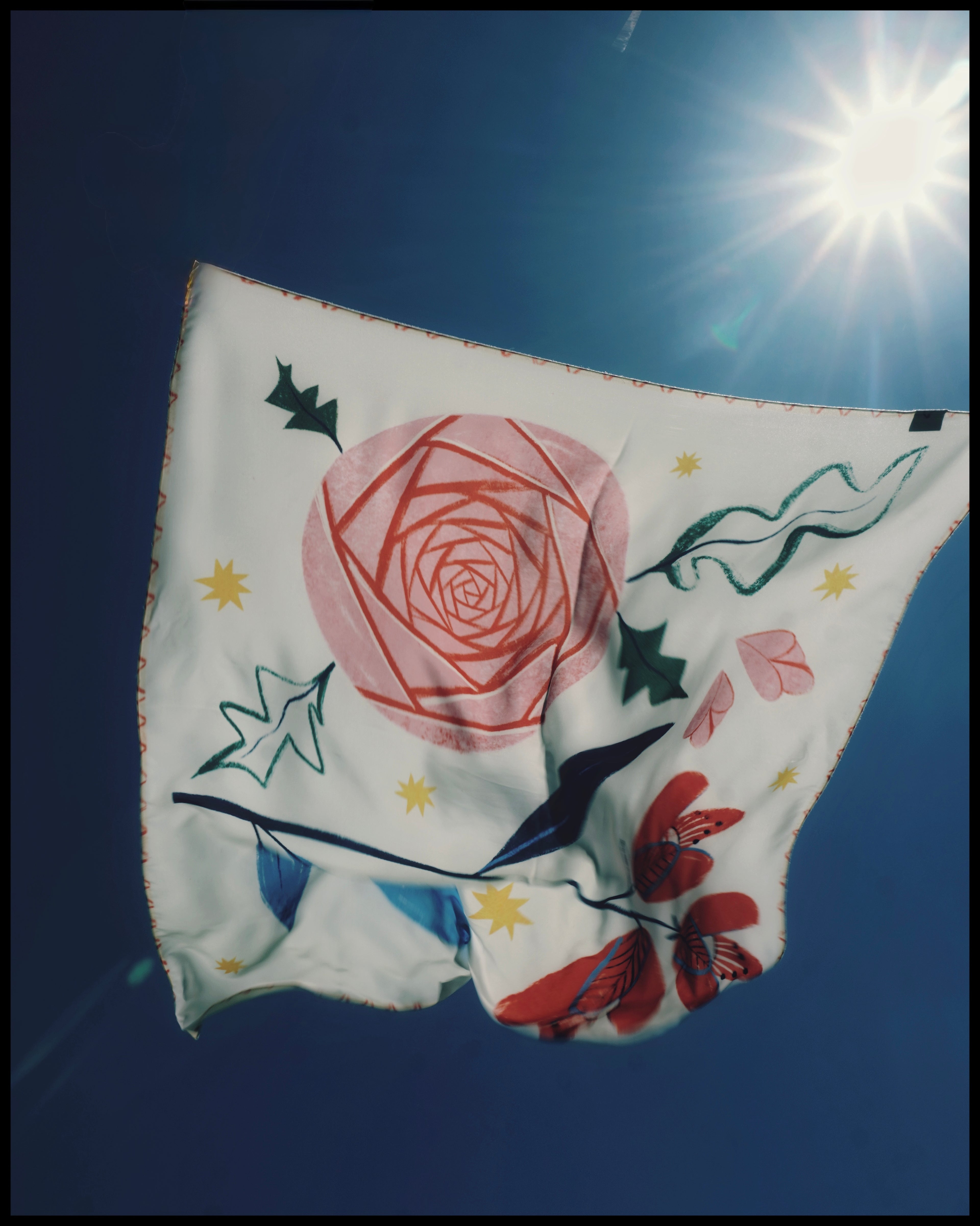 Floral-patterned fabric against a blue sky with sun,  Bloom art silk scarf illustrated by Feli Beringer with roses and symbolic figures