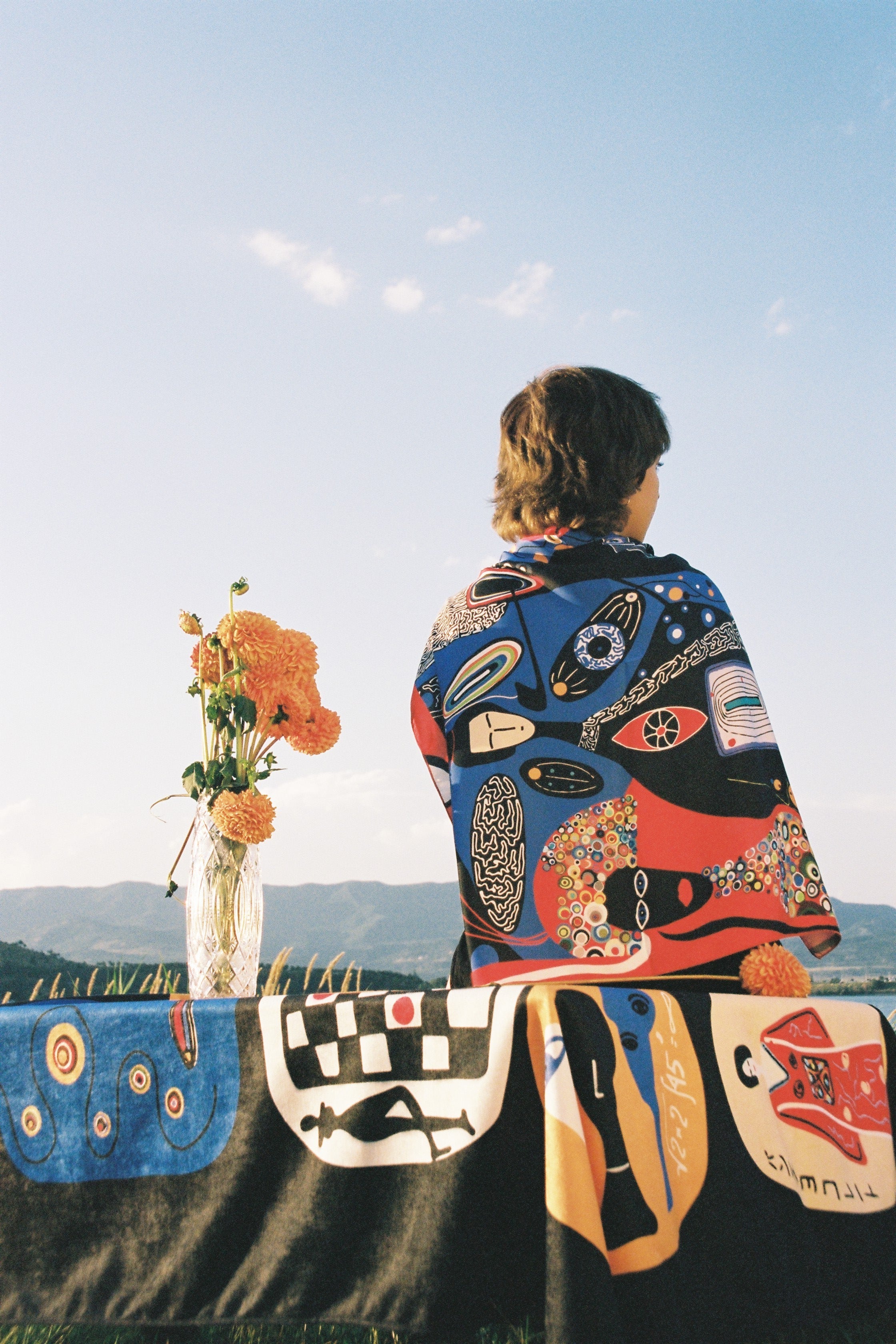 Model styling the Colorful Tale designer scarf. girl wearing it while sitting on the table with tablecloth and flowers