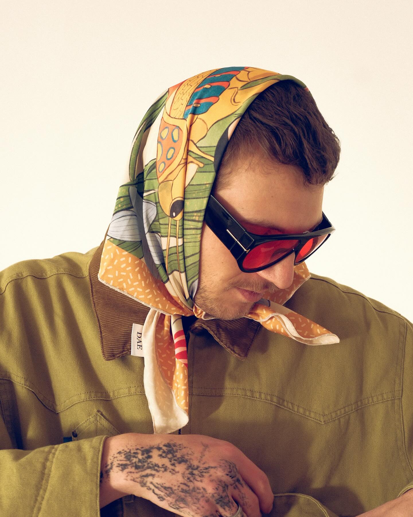 Person wearing a colorful headscarf and sunglasses with a neutral background