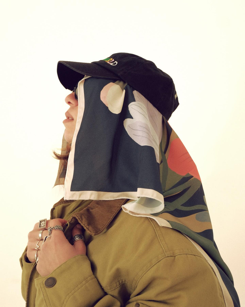 Person wearing a colorful jacket, black cap, and floral scarf on a white background