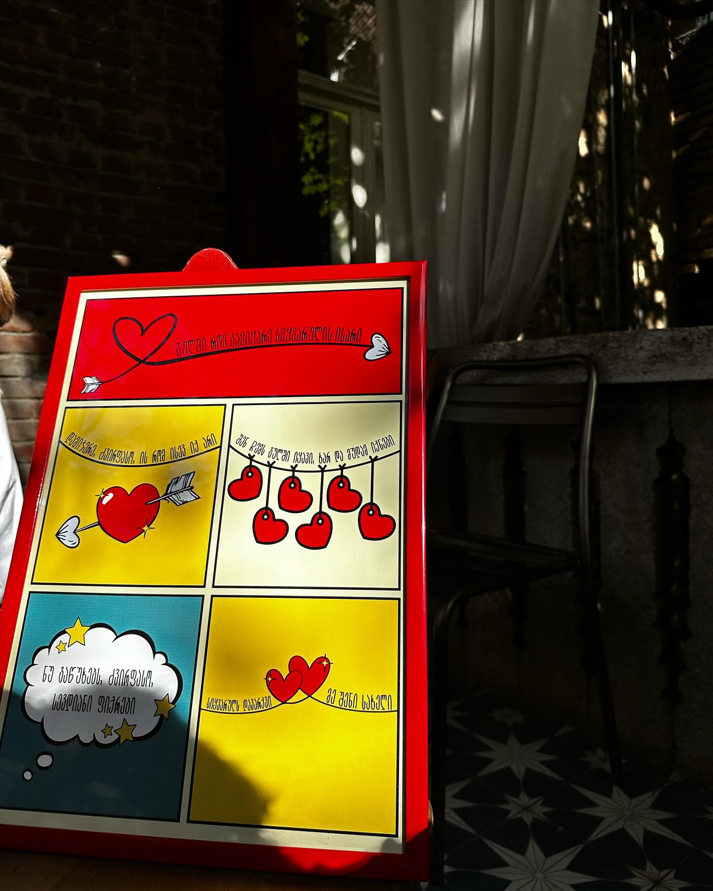 A colorful poster featuring illustrations related to a love theme, with a prominent red heart and the text 'Sikvaruls davarkvi me sheni sakheli'.