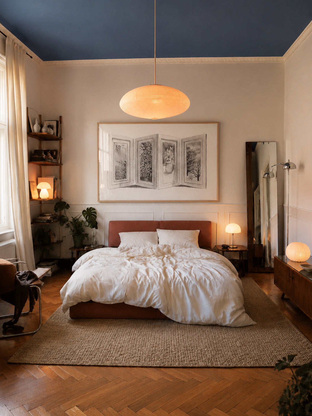 A styled bedroom interior featuring a bed with white bedding, a dark wood headboard, a large woven rug, a blue-painted ceiling, warm pendant lighting, and framed wall art by DAE