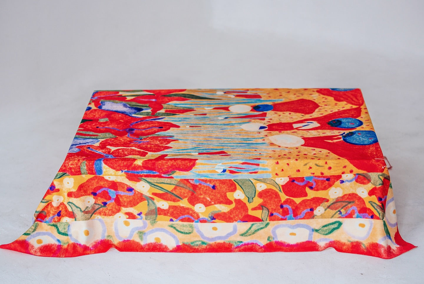 A colorful tablecloth with floral and geometric patterns laid out flat. Designed by Georgian Artist, made by DAE