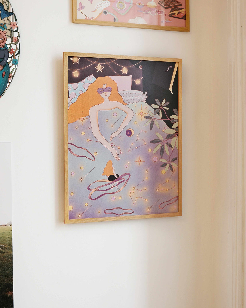 Framed artwork of a woman with orange hair, laying in bed, with stars and dreamy vibe on a white wall.