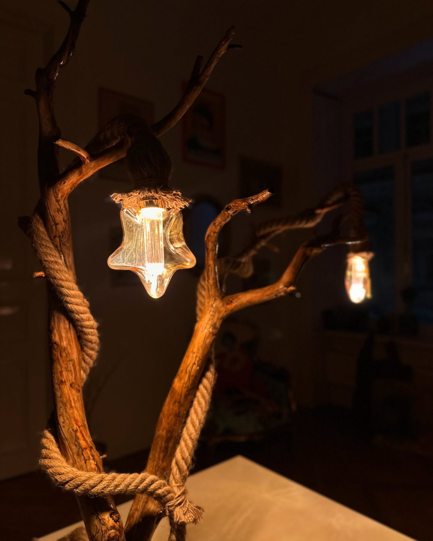 A handmade floor lamp with a branch-like structure and star-shaped glass light covers hanging from it, placed in a dark room.