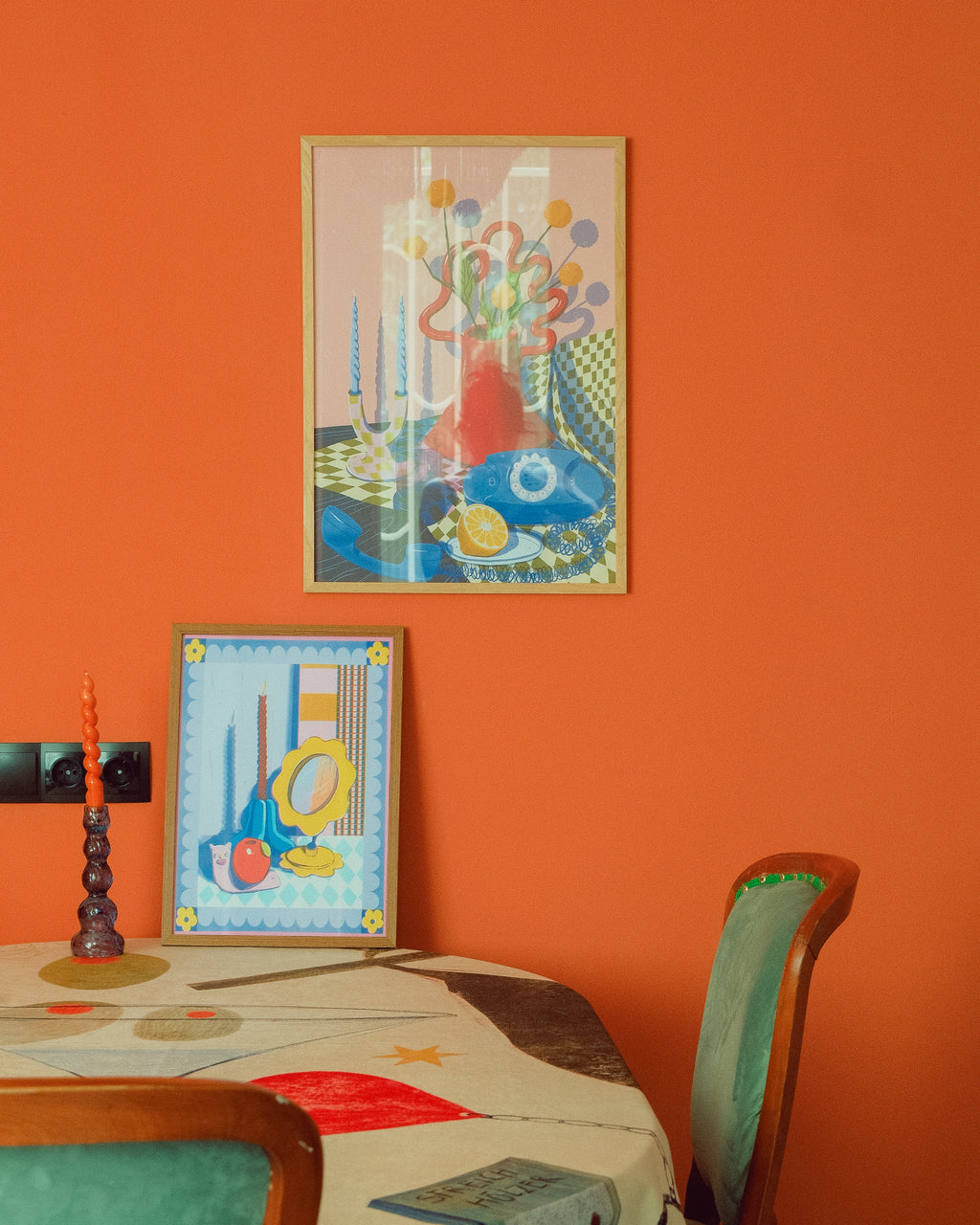 Colorful abstract art on an orange wall with a table and chairs below.