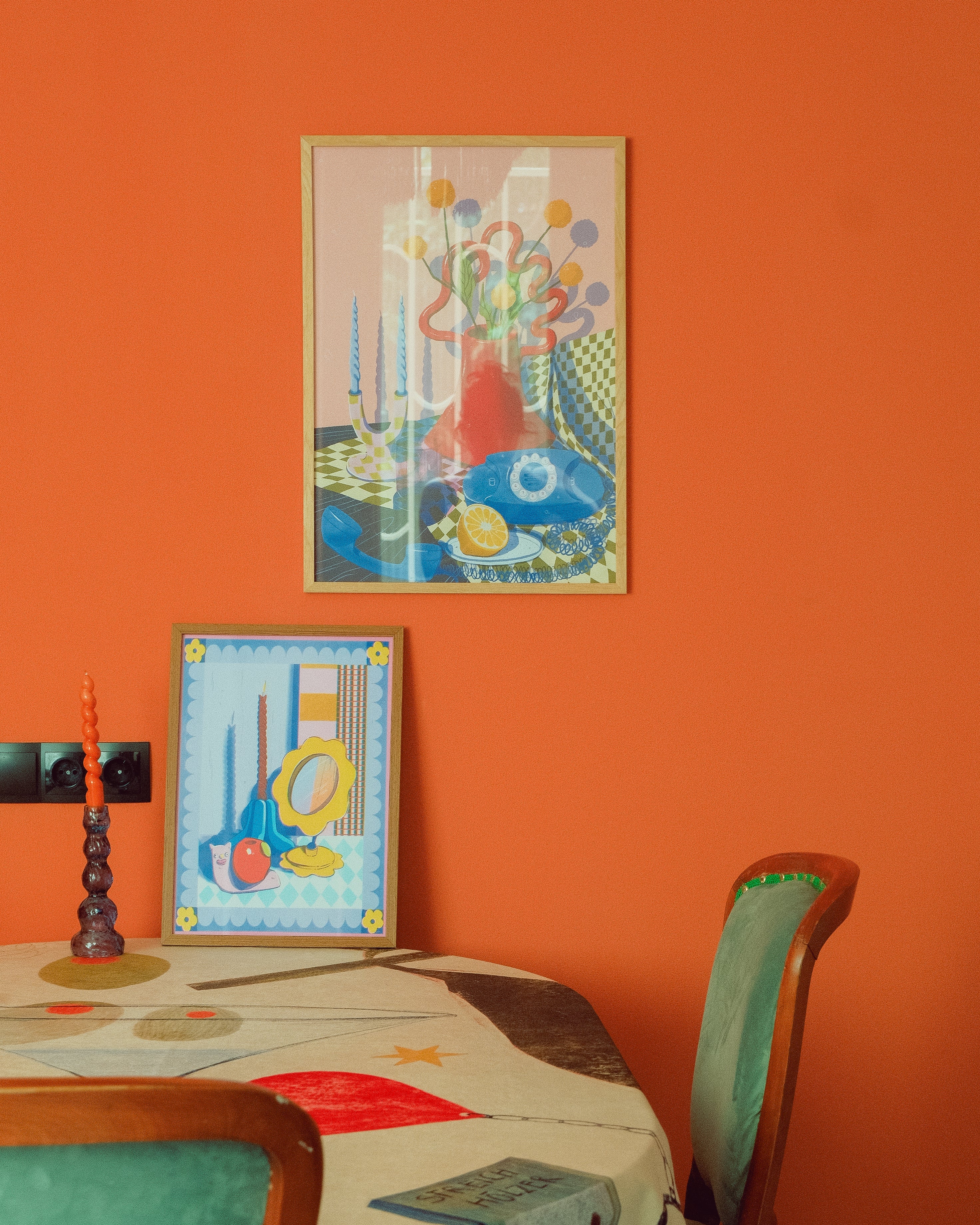 Colorful abstract art on an orange wall with a table and chairs below.