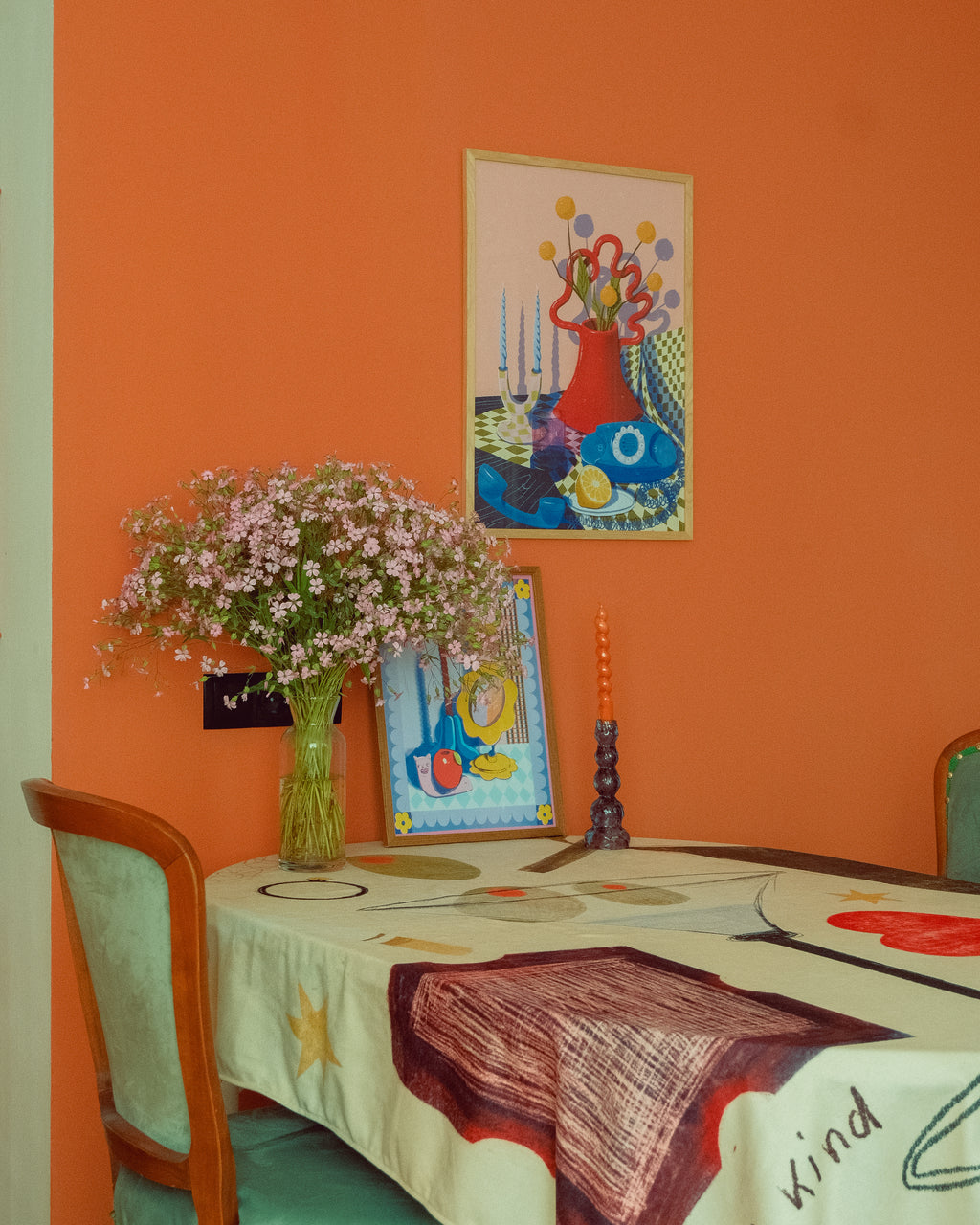 Dining room with orange walls, a tablecloth with abstract designs, and framed posters by DAE