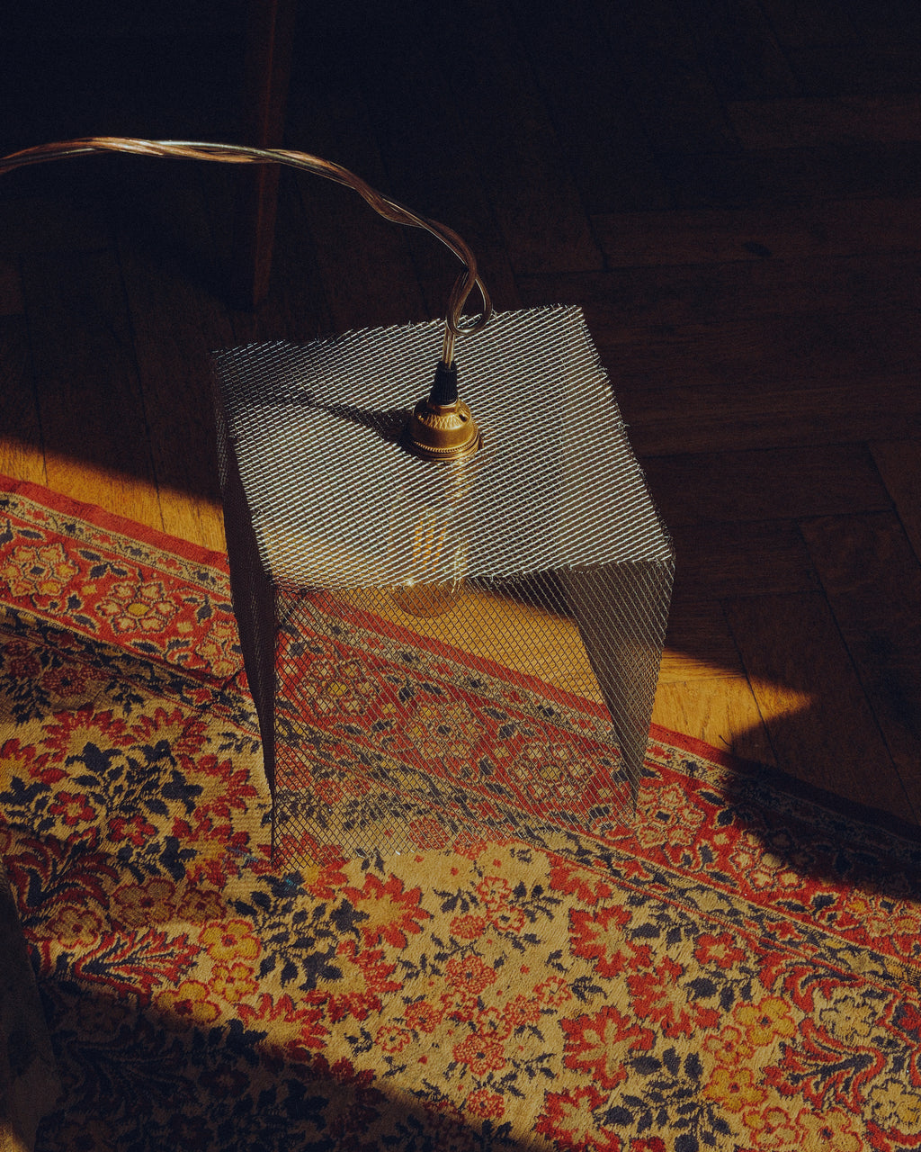 Lifestyle view of the handmade “Loop” lamp, featuring a curved metal structure and suspended mesh shade illuminated over a patterned rug.