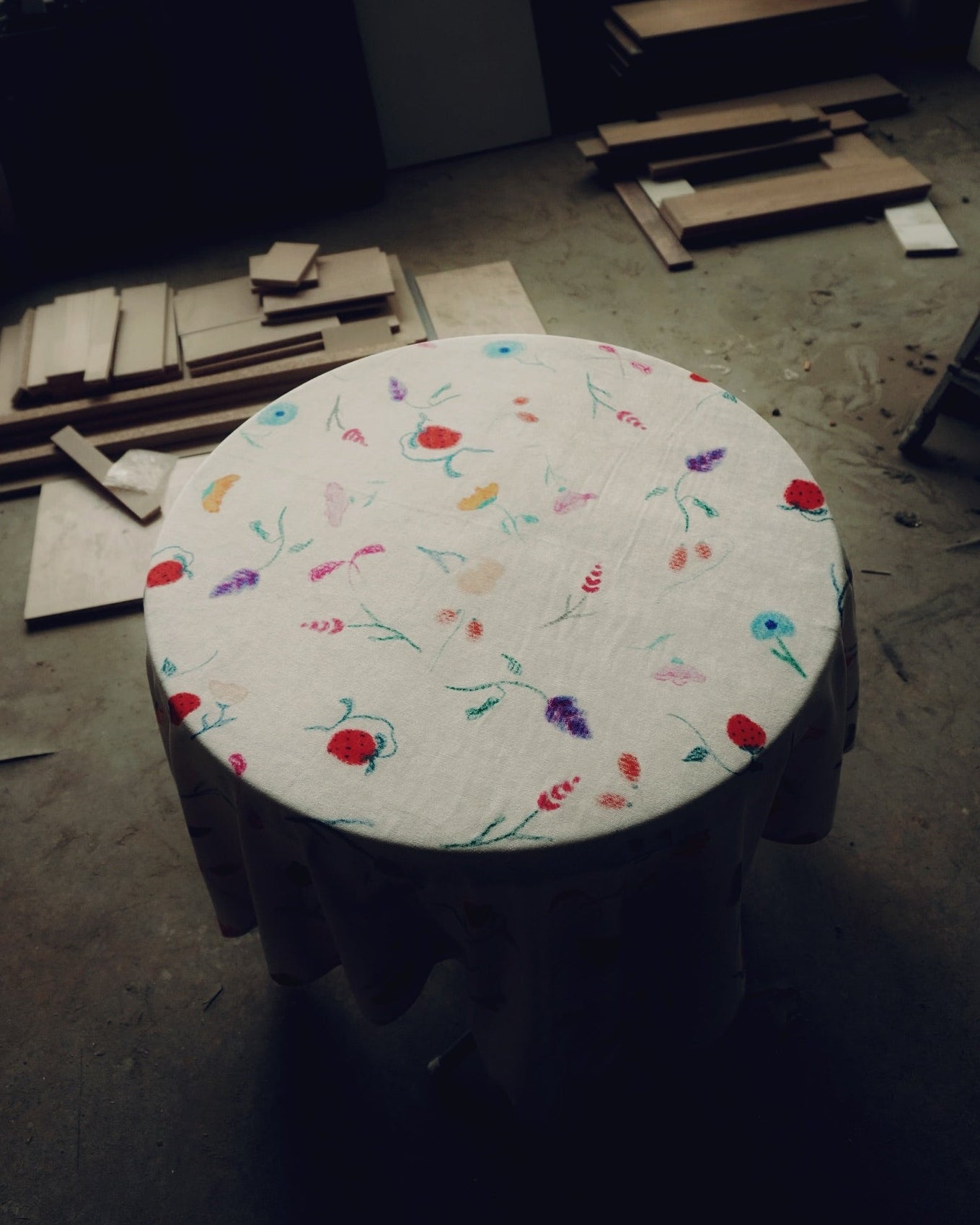 Round table with floral pattern tablecloth on a concrete floor with construction materials.
