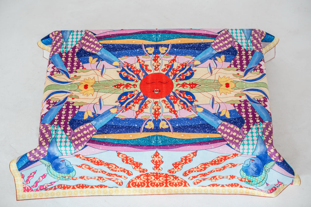 A colorful tablecloth by DAE with a sun-like pattern at the center, featuring geometric shapes and traditional motifs in red, blue, and other colors.