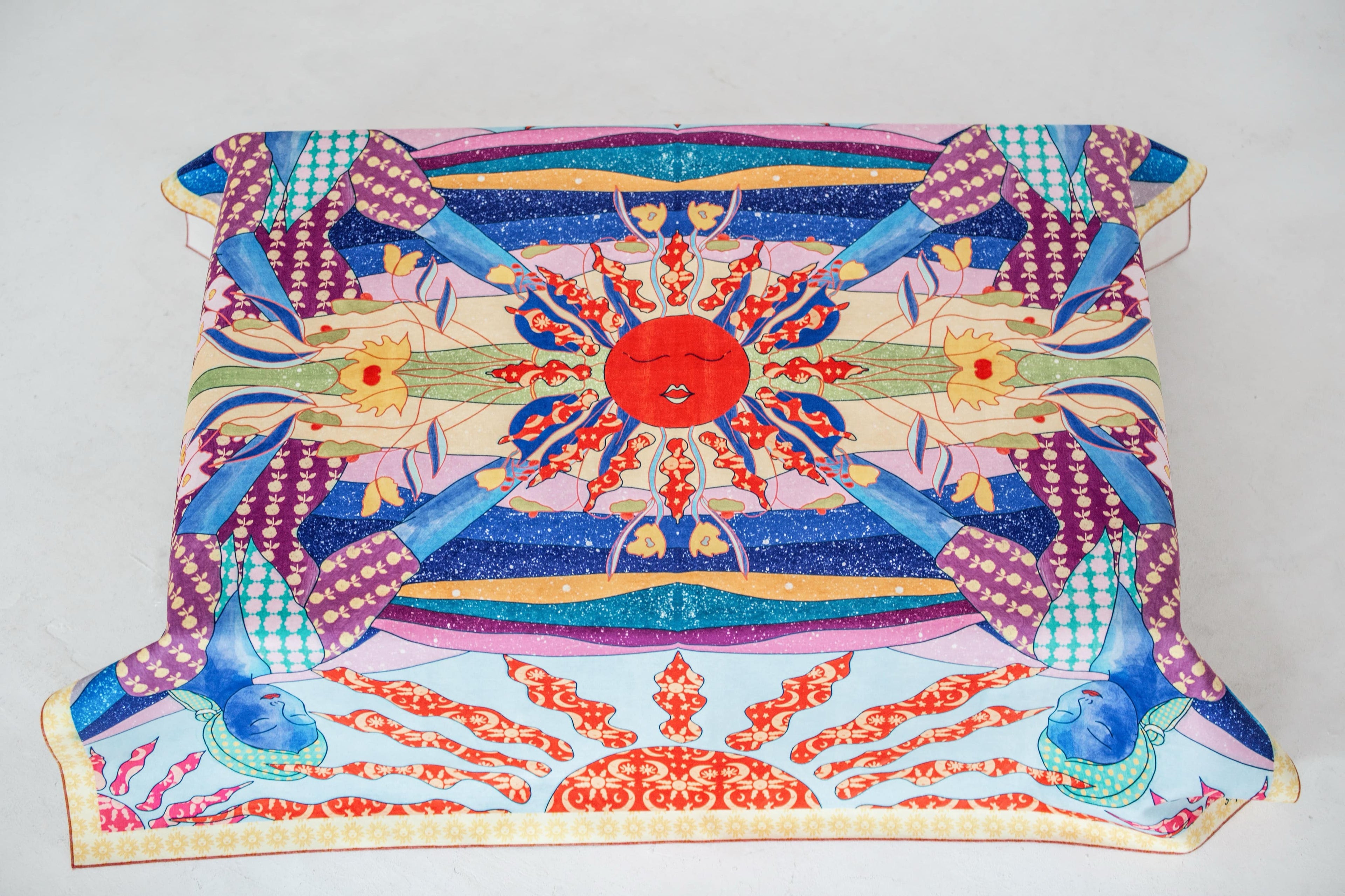 A colorful tablecloth by DAE with a sun-like pattern at the center, featuring geometric shapes and traditional motifs in red, blue, and other colors.