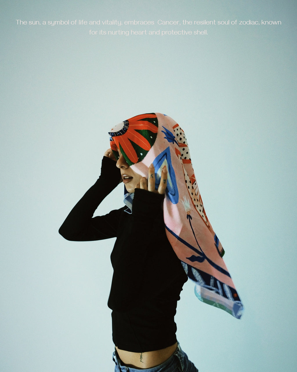 A person wearing a multicolored scarf with a design that includes the sun and cancer symbols.