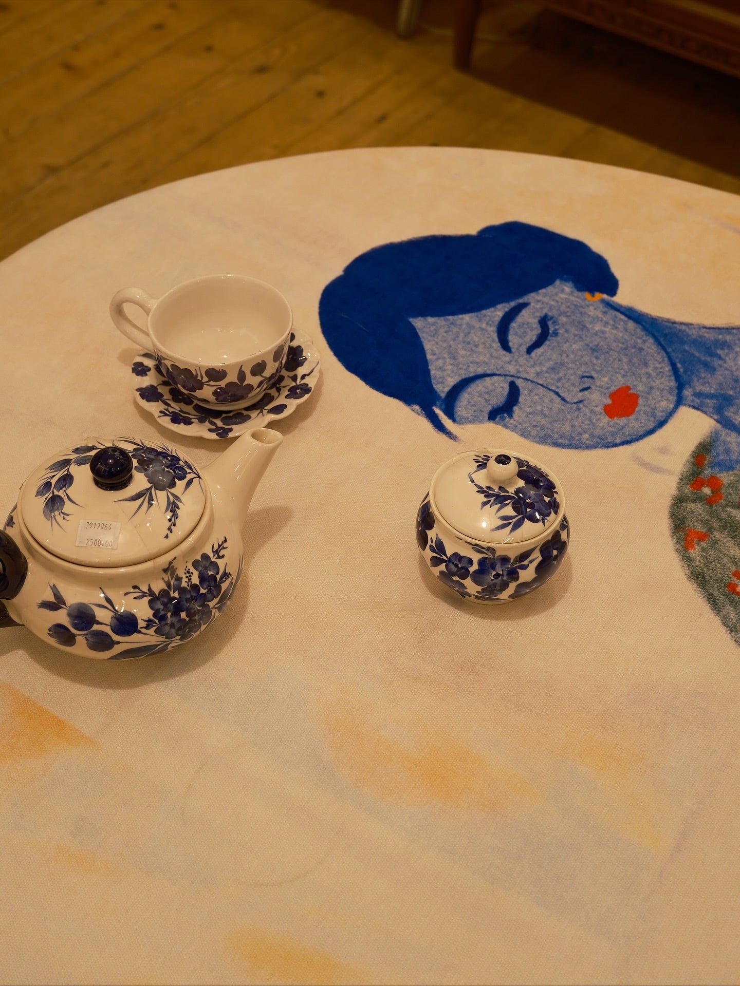 Ceramic teapot, cup, and small container with blue floral patterns on a table with a decorative face design.