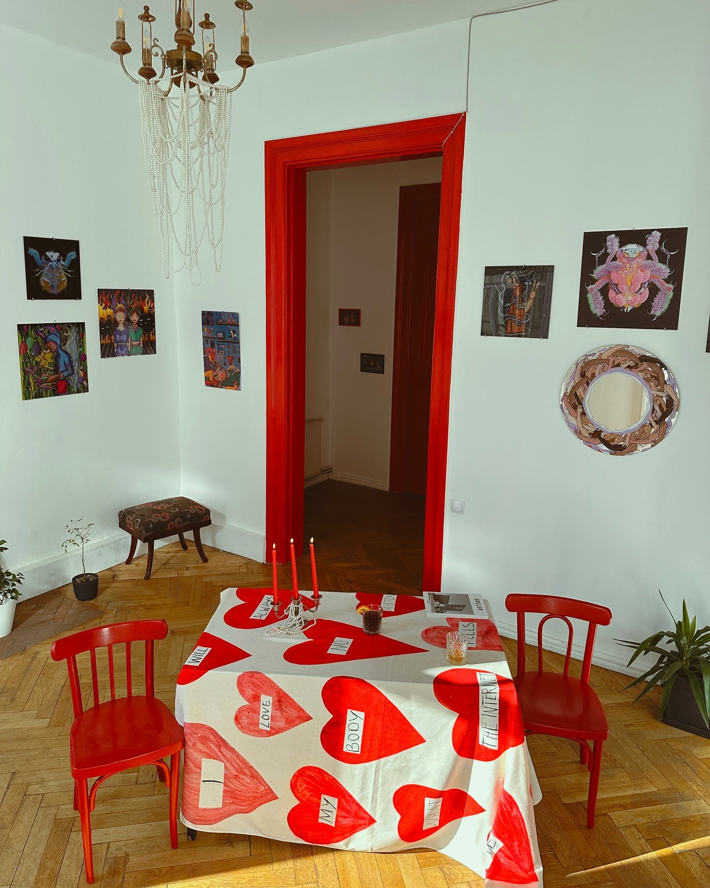 A tablecloth with a red heart pattern displayed on a table in a room with red chairs, white walls, and decorative artwork.