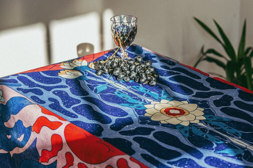 Decorative tablecloth with floral patterns on a table, featuring a glass and small decorative items.