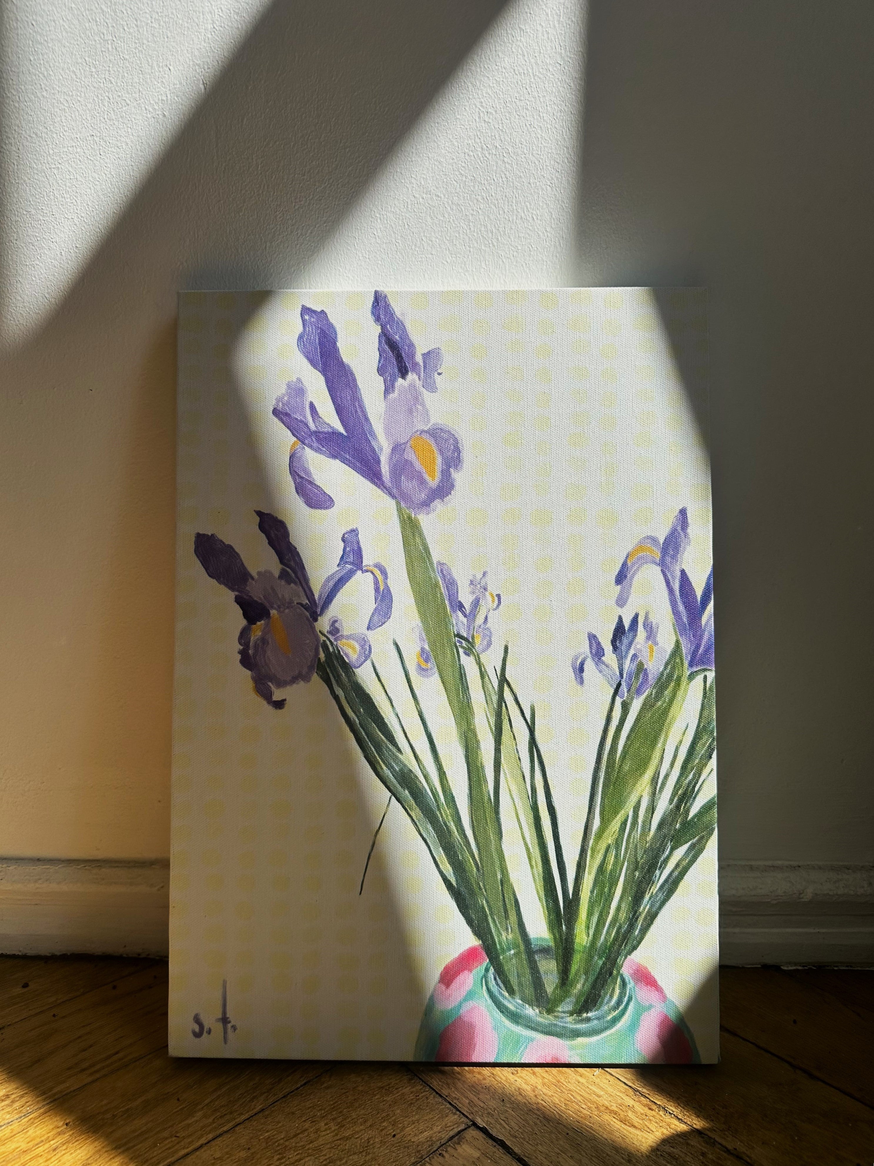 A canvas painting featuring a vase with purple flowers and green leaves, placed against a wall with a patterned background.