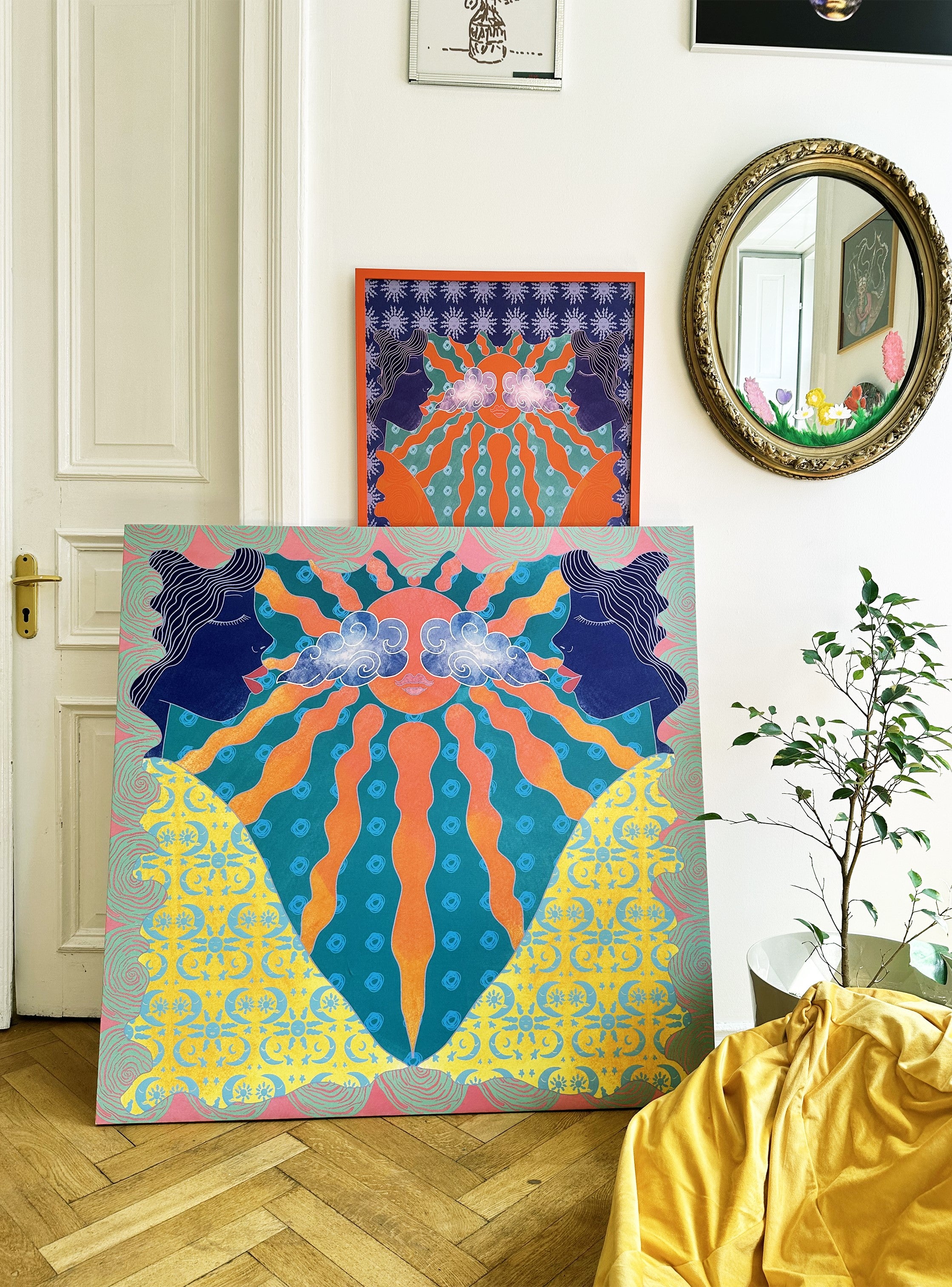 A large canvas artwork, poster by DAE with a geometric and floral pattern, predominantly in blue, orange, and yellow, displayed in a home interior setting.