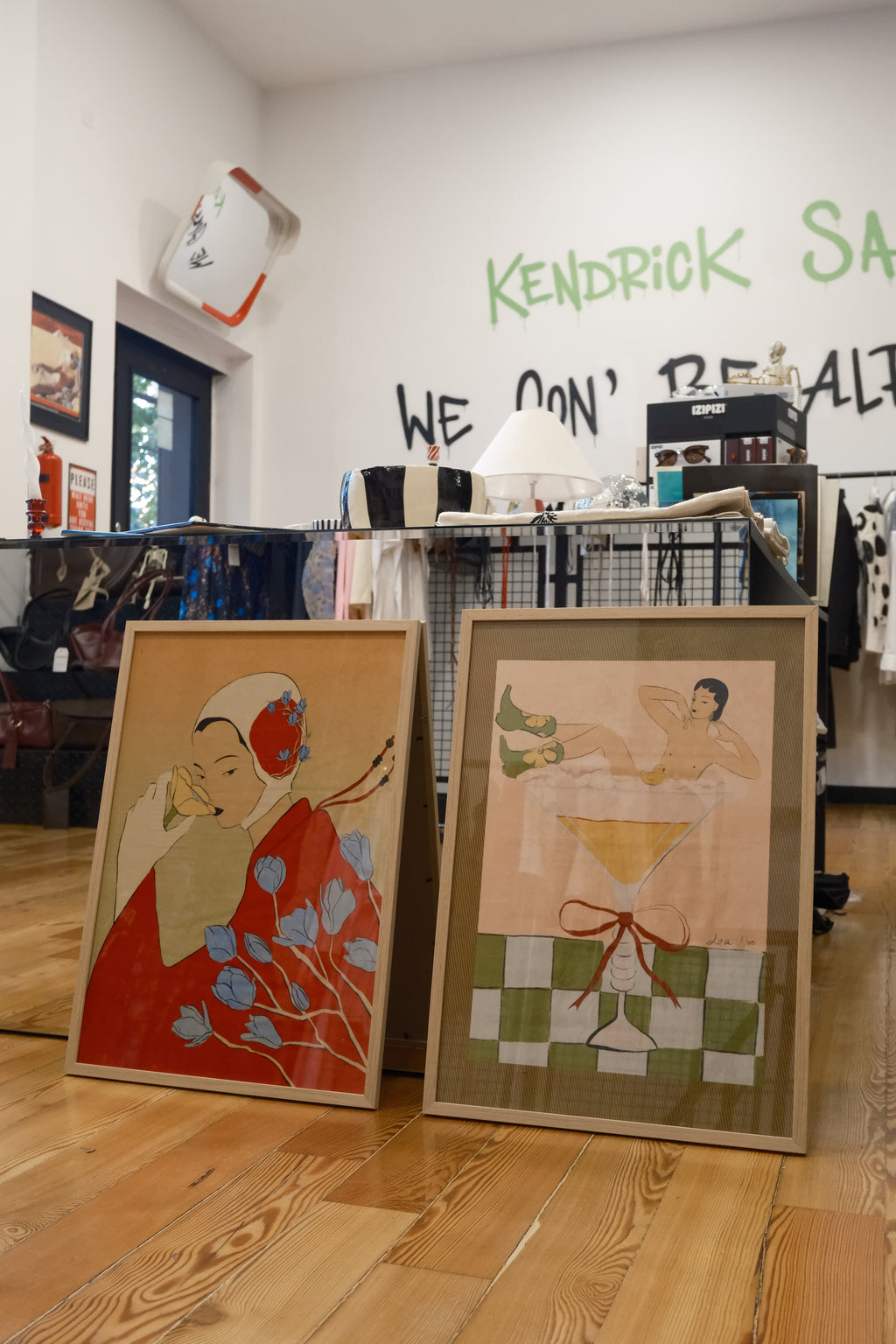 Two framed artworks on a wooden floor with a wall in the background.