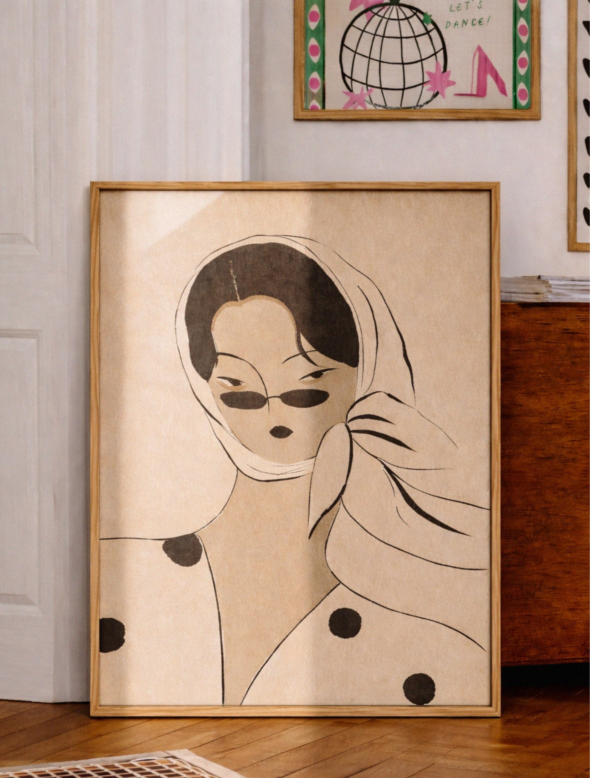 Framed artwork of a stylized woman with a scarf in a room with a painting on the wall.