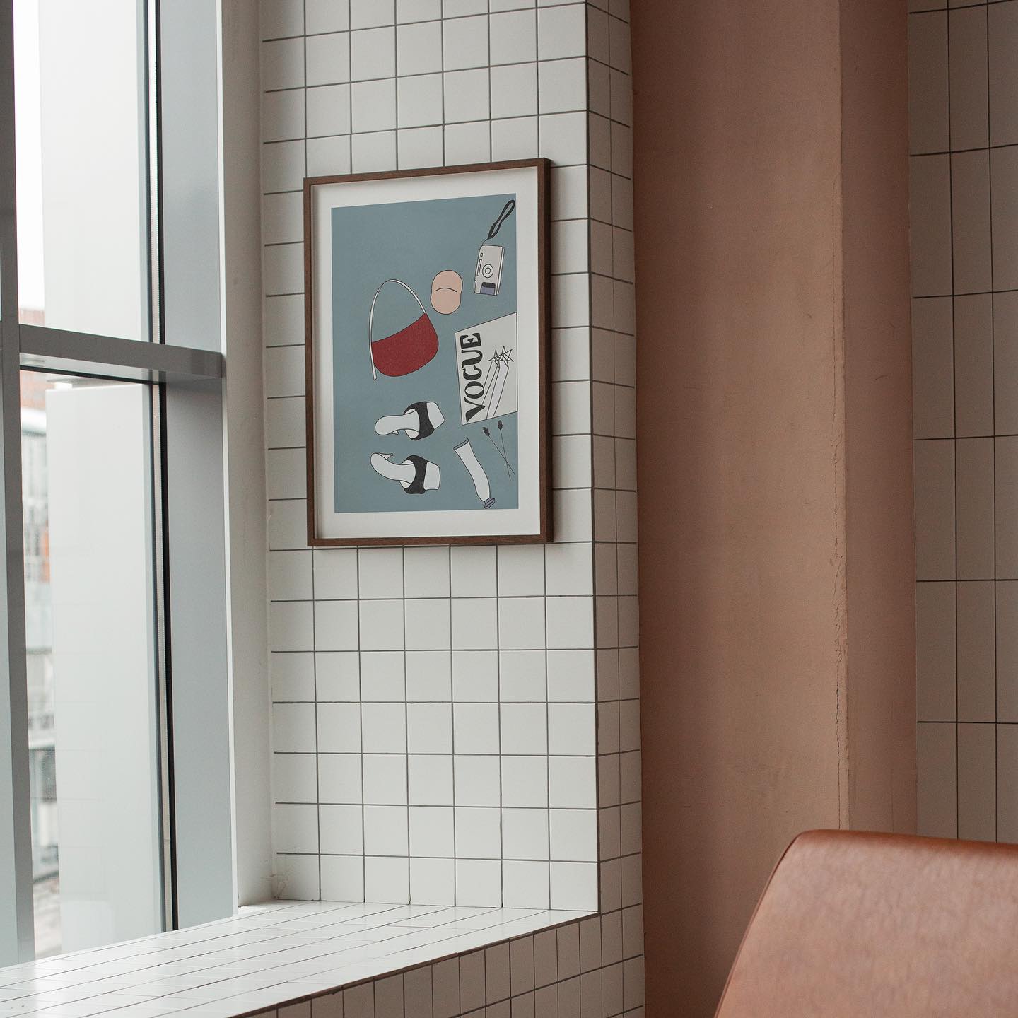 Framed artwork, poster by DAE on a tiled wall next to a window