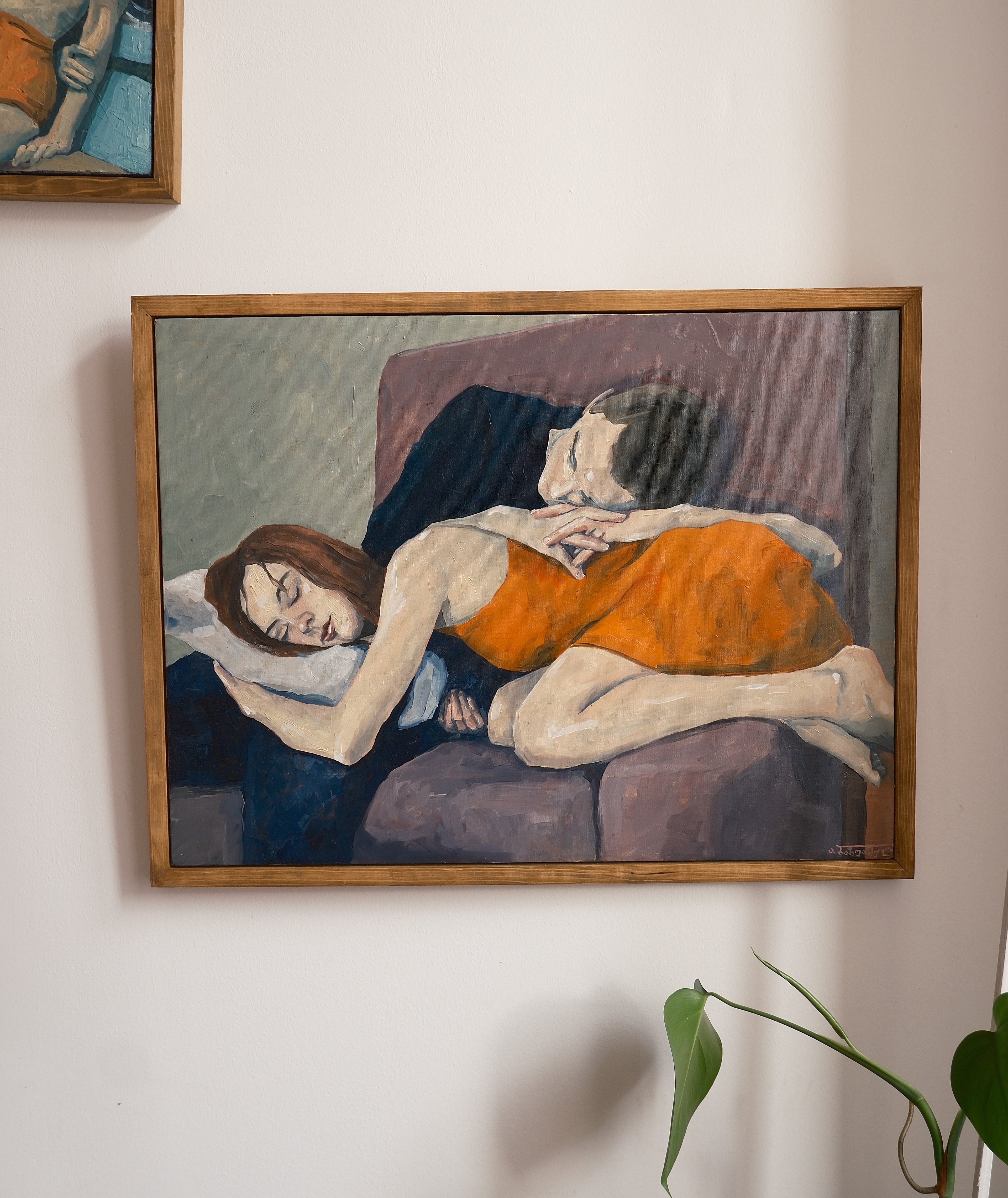 Framed painting of two people embracing on a couch against a white wall.