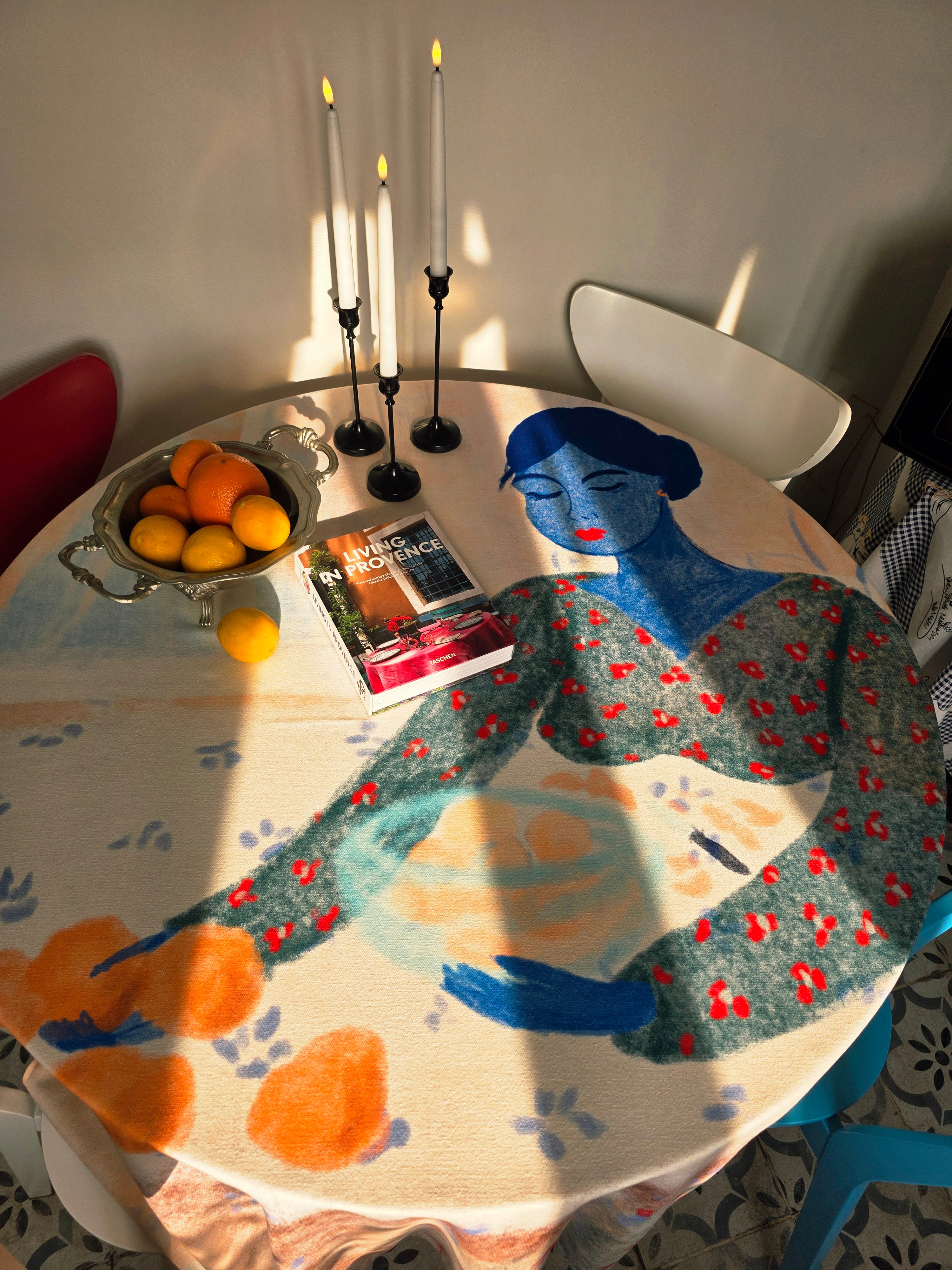 Table with a decorative tablecloth featuring a stylized woman, fruit bowl, and candles.