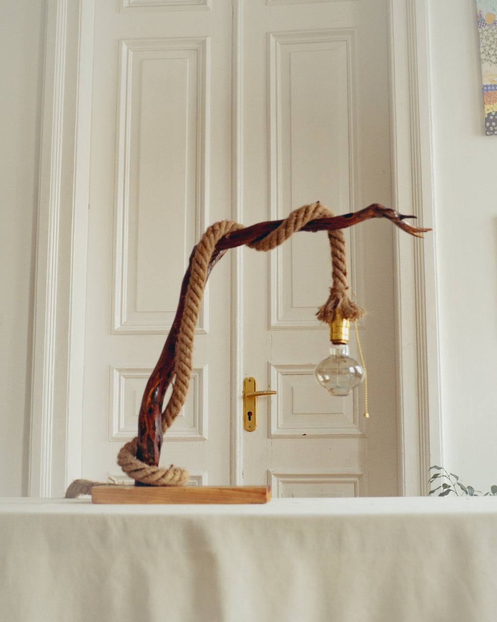Decorative lamp with rope and wooden base against a white paneled wall.