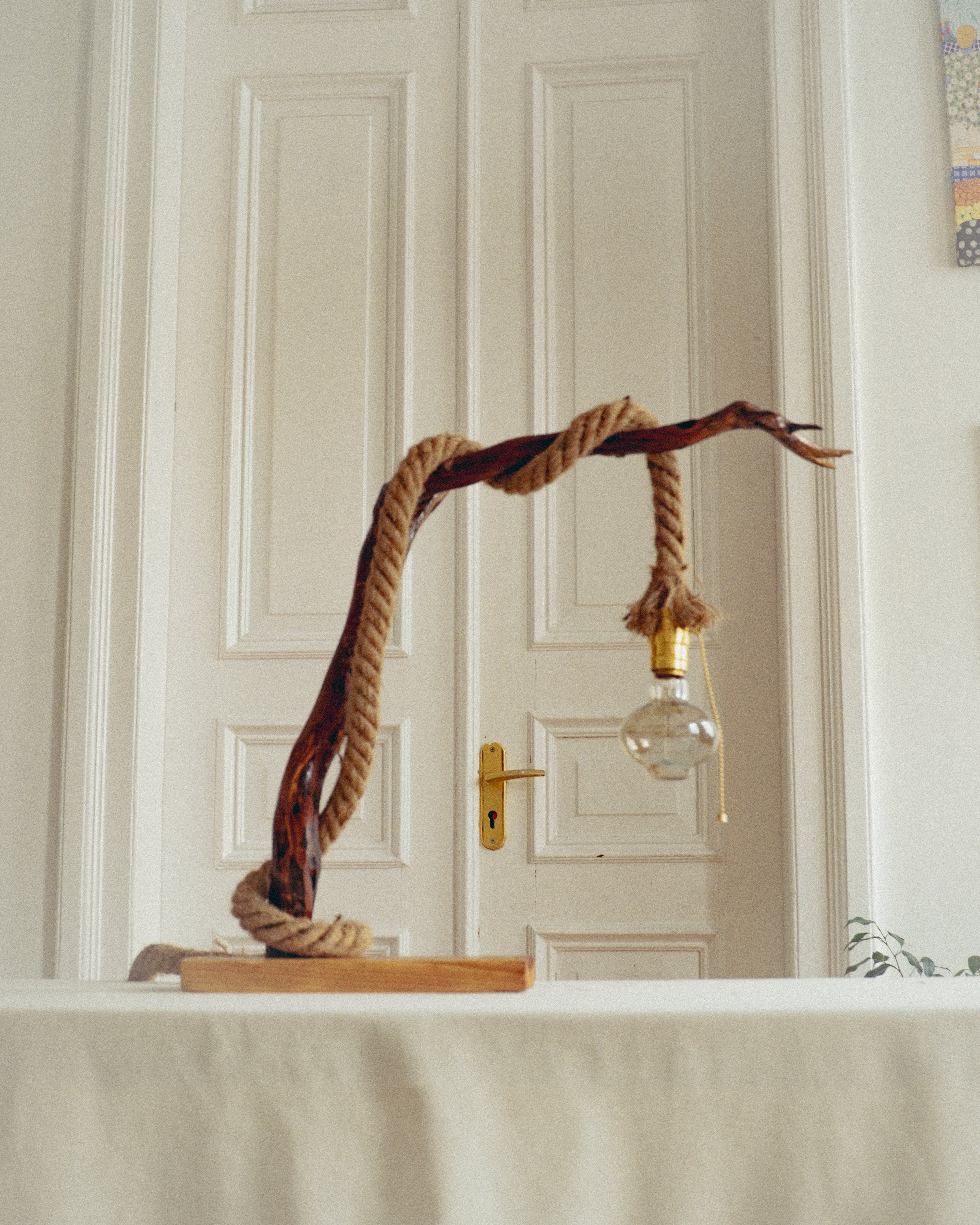 Decorative lamp with rope and wooden base against a white paneled wall.